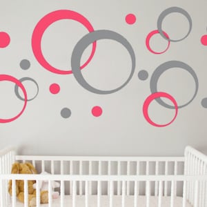 May include: A nursery wall decorated with pink and gray circles of varying sizes. The circles are arranged in a random pattern and create a modern and playful design.