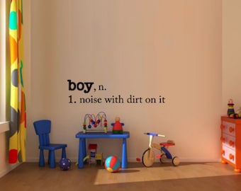 May include: A nursery wall decal with the word "boy" defined as "noise with dirt on it". The decal is on a white wall with a colorful curtain in the background. There are toys in the foreground, including a blue toy chair, a tricycle, and a toy playset.