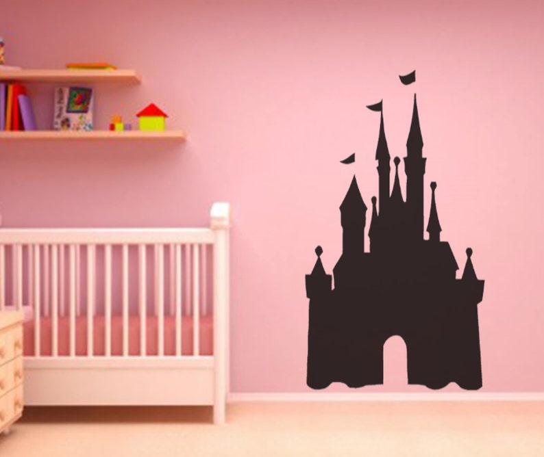 May include: A black silhouette of a fairytale castle on a pink wall. The castle has many towers and a large arched entrance. The silhouette is a wall decal.