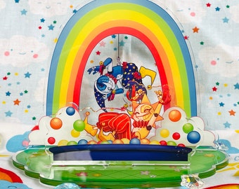 May include: A colorful acrylic stand with a rainbow arch, two cartoon characters, and a blue pool of water with white and red balls. The characters are a blue and white jester and a yellow jester with red and white clothing.