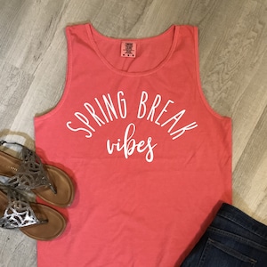 May include: A coral-colored tank top with the text "Spring Break vibes" printed in white.