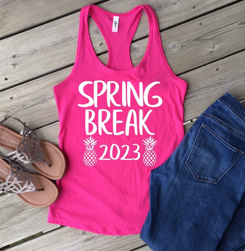 May include: Pink tank top with white text that says "Spring Break 2023" and two white pineapple graphics.
