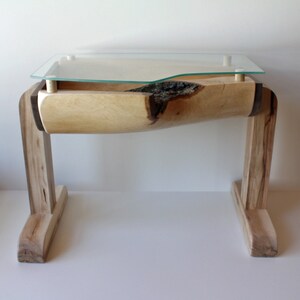 May include: A wooden table with a curved top and a glass top. The table is made of light wood and has a natural finish. The legs are made of dark wood and have a simple design.