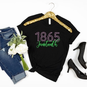 May include: Black t-shirt with the text "1865 Juneteenth" in green and pink lettering.