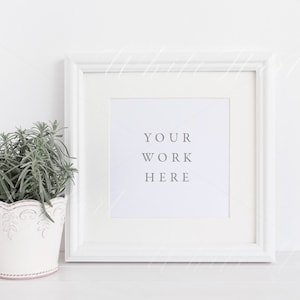 Peut inclure: Cadre photo blanc avec un passe-partout blanc et le texte "YOUR WORK HERE" sur un fond blanc. Une petite plante en pot se trouve à gauche du cadre.
