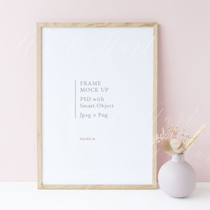 Puede incluir: Una maqueta de marco de madera con fondo blanco y el texto "FRAME MOCK UP PSD with Smart Object Jpeg + Png 30x40cm". El marco est&aacute; colocado sobre una superficie blanca frente a una pared rosa claro. Un jarr&oacute;n con flores secas est&aacute; a la derecha del marco.