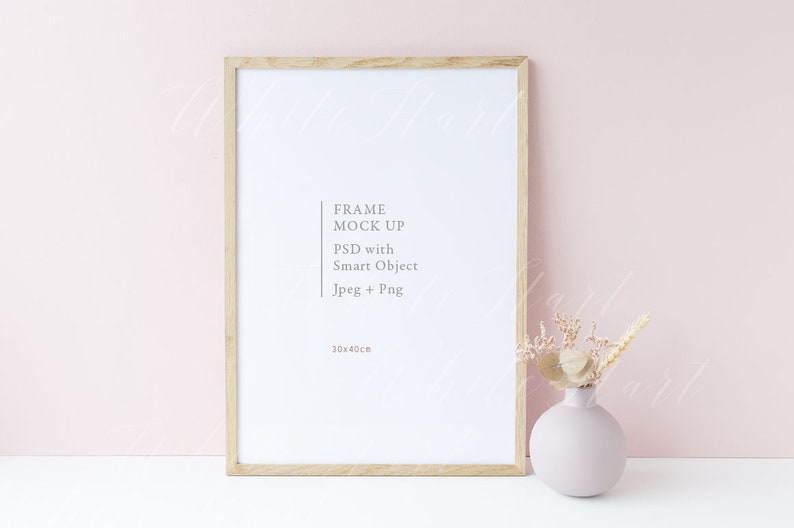 Puede incluir: Una maqueta de marco de madera con fondo blanco y el texto "FRAME MOCK UP PSD with Smart Object Jpeg + Png 30x40cm". El marco est&aacute; colocado sobre una superficie blanca frente a una pared rosa claro. Un jarr&oacute;n con flores secas est&aacute; a la derecha del marco.