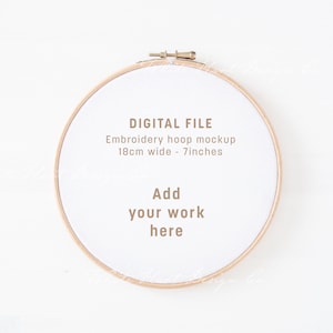 Könnte beinhalten: Ein weißer Stickrahmen mit einem Holzrahmen und einem beigefarbenen Stoffzentrum. Der Rahmen ist 18 cm breit und hat den Text "DIGITAL FILE Embroidery hoop mockup 18cm wide - 7 inches Add your work here" auf dem Stoff gedruckt.