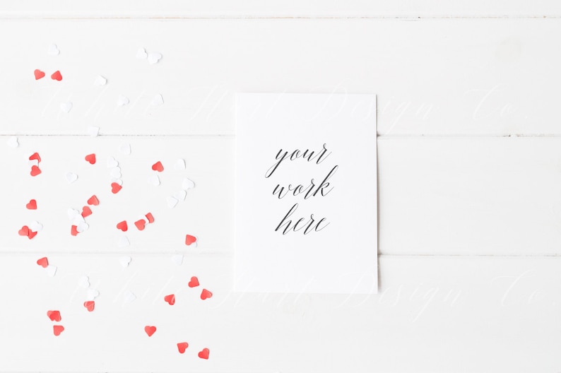 Puede incluir: Una tarjeta blanca con el texto "your work here" escrito en caligraf&iacute;a negra, sobre un fondo de madera blanca con confeti en forma de coraz&oacute;n rojo y blanco esparcidos alrededor de la tarjeta.