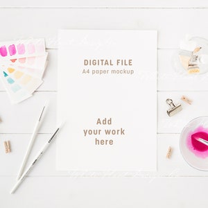 May include: A white A4 paper mockup with the text "DIGITAL FILE A4 paper mockup Add your work here" on a white wooden table with paintbrushes, paint tubes, and a watercolor palette.