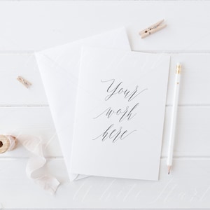 K&ouml;nnte beinhalten: Eine wei&szlig;e Karte mit dem Text "Your work here" in schwarzer Kalligraphie. Die Karte liegt auf einer wei&szlig;en Holzoberfl&auml;che mit einem wei&szlig;en Umschlag, einem Bleistift und einer Spule wei&szlig;en Bandes.