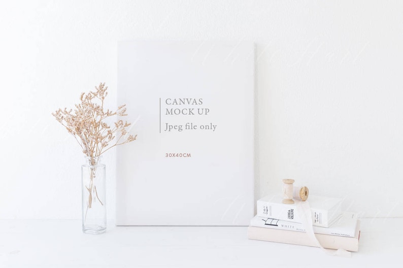 May include: White canvas mock-up with the text "Canvas Mock Up Jpeg file only 30x40CM" on a white background. A vase with dried flowers and a spool of thread are on a white surface in front of the canvas.