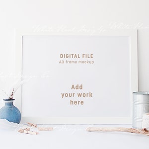 Puede incluir: Maqueta de marco blanco con el texto "DIGITAL FILE" y "A3 frame mockup". El texto "Add your work here" también está incluido en el marco. El marco está sentado sobre una superficie blanca con un jarrón azul, un palo de madera, una lata de metal y cuerda.