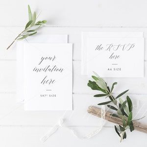 May include: Two white cards on a white wooden background with green sprigs. The larger card says "your invitation here 5x7" size. The smaller card says "the RSVP here A6 size".