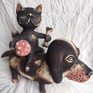 Keramikkatze reitet auf einem Keramikhund mit einem Ball und einem Knochen