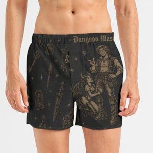 Könnte beinhalten: Schwarze Boxershorts mit einem goldfarbenen Aufdruck von Fantasy-Motiven wie einem Schlüssel, einem Dolch und einer Truhe. Der Bund trägt den Schriftzug "Dungeon Master" und der Stoff zeigt eine Figur, die neben einem geflügelten Wesen steht.