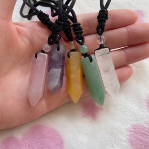 May include: Five crystal point pendants on black cords. The pendants are in the colors pink, purple, yellow, green, and clear.