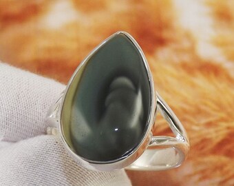 Könnte beinhalten: Ein tropfenförmiger Ring mit einem dunkelgrünen und grauen Edelstein, der in eine silberne Fassung gefasst ist.