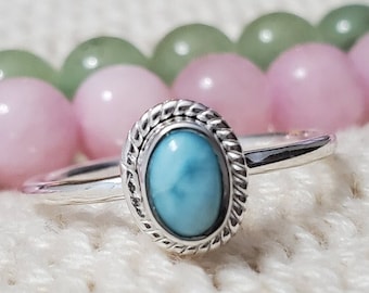 May include: A silver ring featuring a blue oval gemstone set in a silver bezel. The ring is encircled by a rope-like design.