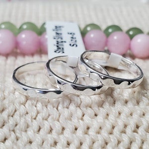 Op de afbeelding: Drie ringen van sterling zilver met een gehamerde, geschulpte randtextuur. Elke ring heeft een gepolijste, reflecterende afwerking. Een wit rechthoekig label is bevestigd met de tekst Sterling Silver Ring Size 6 duidelijk afgedrukt.