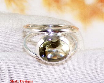 Puede incluir: Un anillo de plata con una gran piedra preciosa ovalada de color verde claro. El anillo tiene un diseño de caña dividida, con la banda dividiéndose en dos líneas paralelas que se curvan alrededor de la piedra preciosa. El texto "Shalz Designs" es visible.
