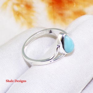 May include: A silver ring featuring a light blue teardrop-shaped gemstone. The ring has a simple, elegant design.