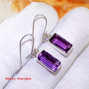 May include: A pair of sterling silver earrings featuring rectangular amethyst gemstones. The earrings have a simple, elegant design and are ideal for everyday wear.
