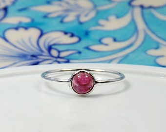 May include: A silver ring with a pink oval gemstone set in a bezel setting.