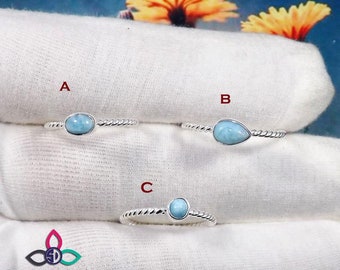 May include: Three silver rings with blue gemstone settings. The rings are labeled A, B, and C. The rings are on a white fabric background.