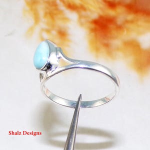 May include: A silver ring featuring a light blue oval gemstone. The ring has a simple design with a delicate band.