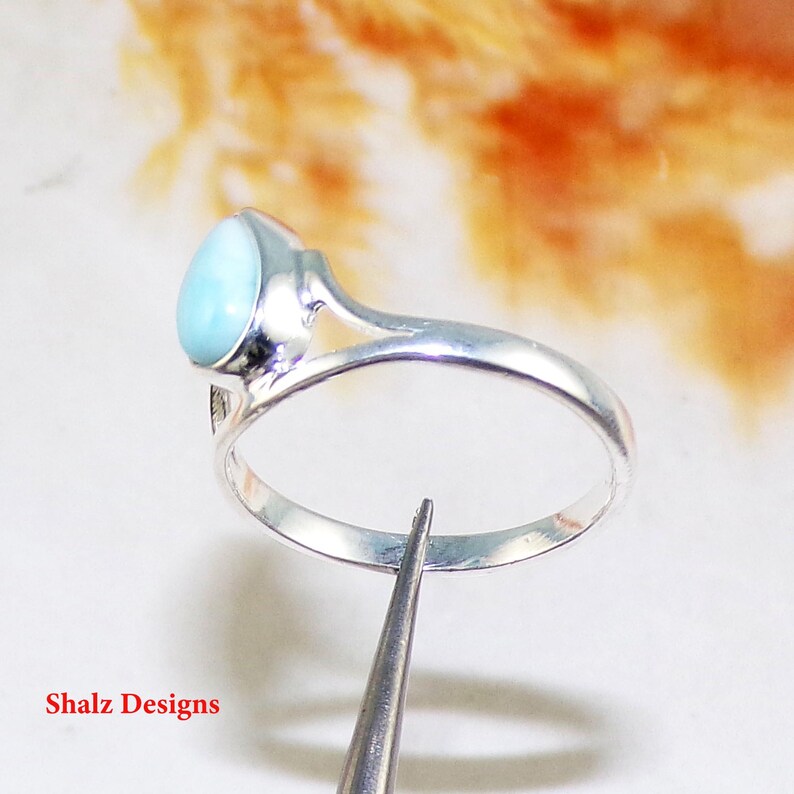May include: A silver ring featuring a light blue oval gemstone. The ring has a simple design with a delicate band.