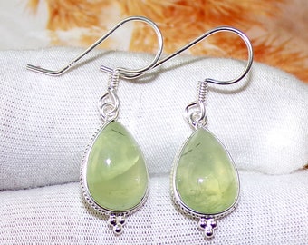 May include: A pair of silver dangle earrings with green teardrop-shaped stones. The stones have a translucent, cloudy appearance with a hint of sparkle.