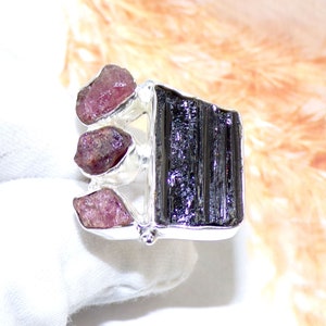 May include: A silver ring featuring a black tourmaline gemstone and three pink tourmaline gemstones.