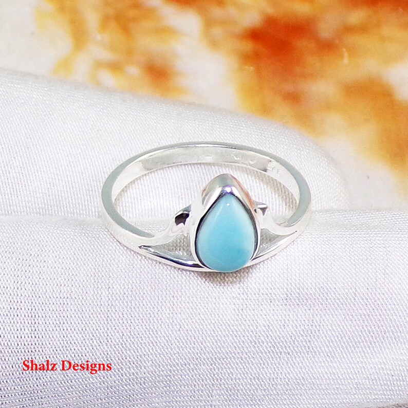 May include: A silver ring featuring a teardrop-shaped blue gemstone set in a delicate, openwork design.