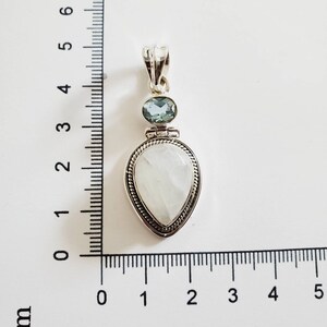 May include: A silver pendant with a white moonstone and a light blue aquamarine gemstone. The pendant is approximately 2 cm in length.