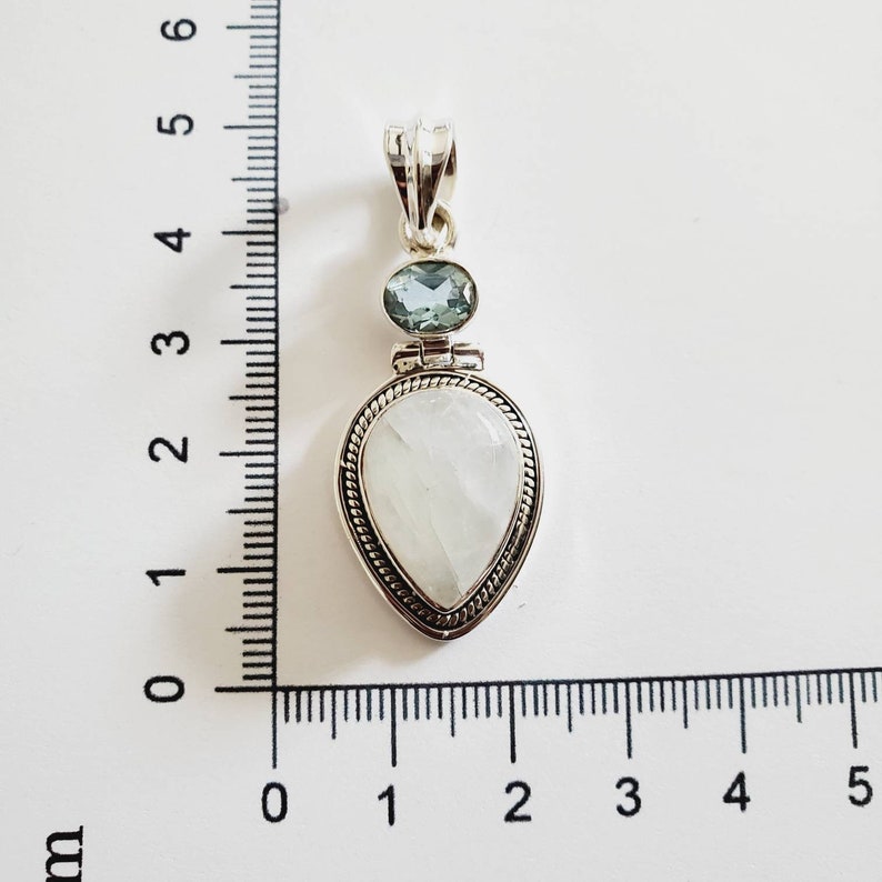 May include: A silver pendant with a white moonstone and a light blue aquamarine gemstone. The pendant is approximately 2 cm in length.