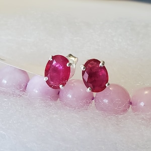 May include: A pair of silver stud earrings with oval-shaped red ruby gemstones.