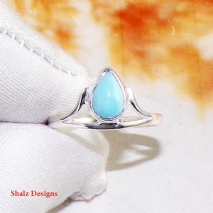 May include: A silver ring featuring a teardrop-shaped turquoise gemstone. The ring has a delicate design with curved lines.