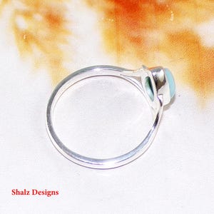May include: A silver ring with a light blue oval gemstone set in a bezel setting.
