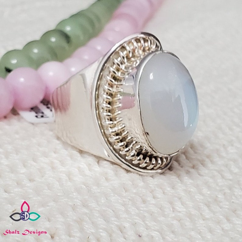 Puede incluir: Un anillo de plata con una piedra de luna blanca engastada en un dise&ntilde;o de alambre retorcido.