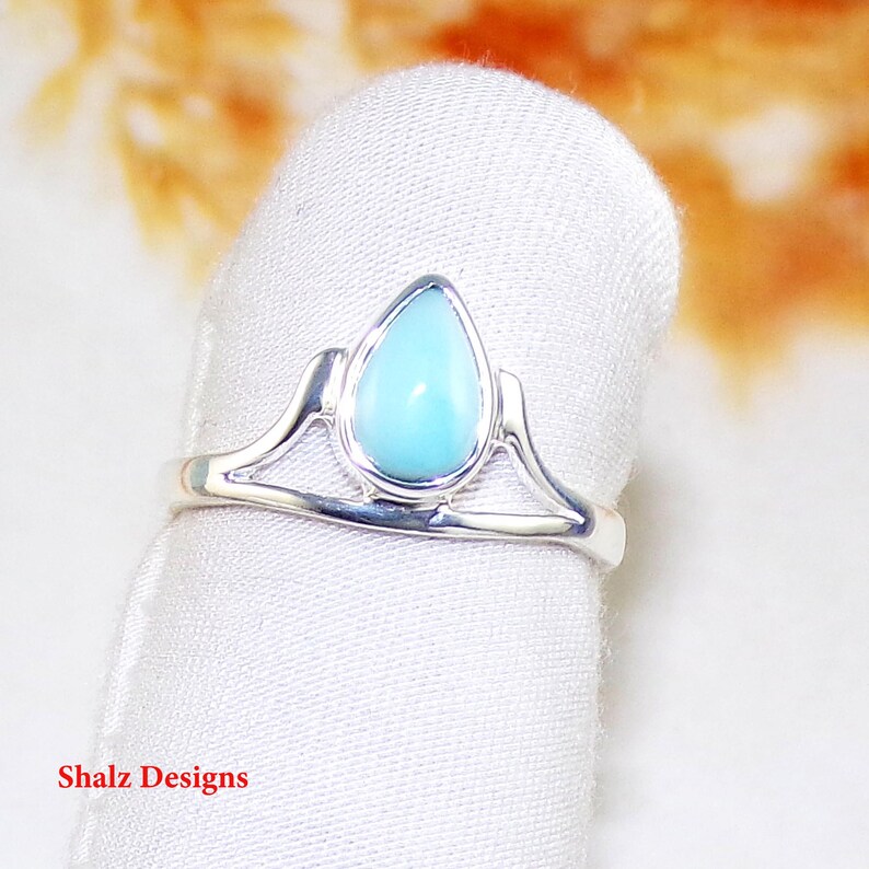 May include: A silver ring featuring a teardrop-shaped turquoise gemstone. The ring has a delicate design with two curved lines on either side of the stone.