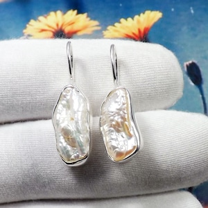 Peut inclure: Une paire de boucles d'oreilles pendantes en argent avec des gouttes de perles baroques blanches. Les perles sont de forme irrégulière et ont un aspect naturel et organique.