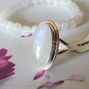May include: A silver ring featuring a large oval moonstone set in a silver bezel. The ring has a textured band and a small row of gold beads on the side.
