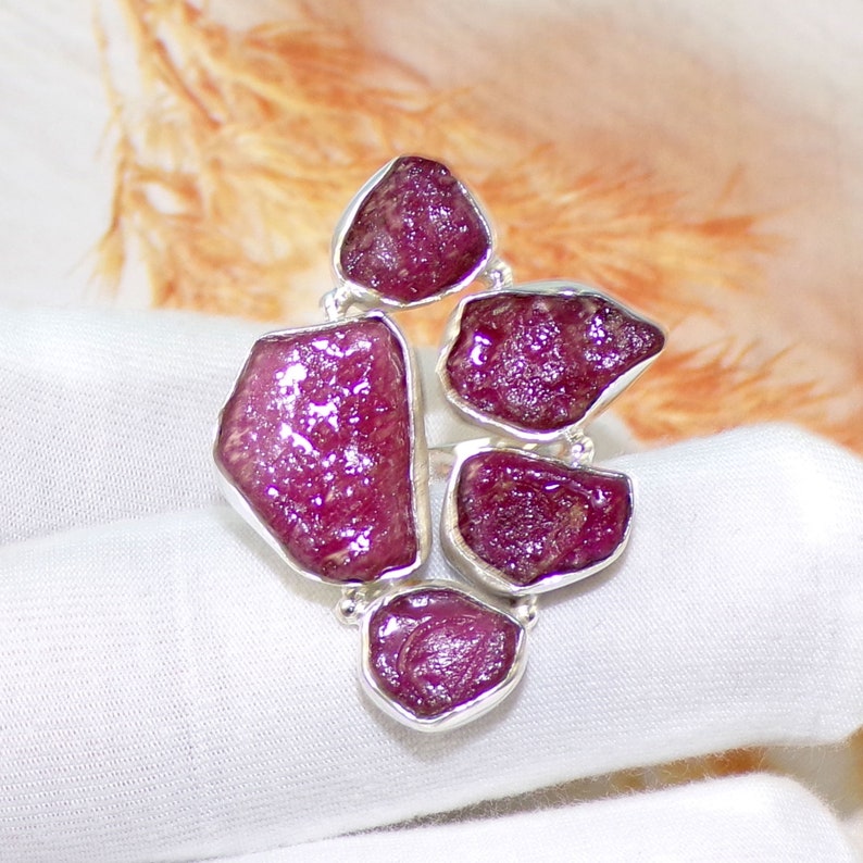 May include: A silver ring with five pink ruby gemstones set in a cluster design.