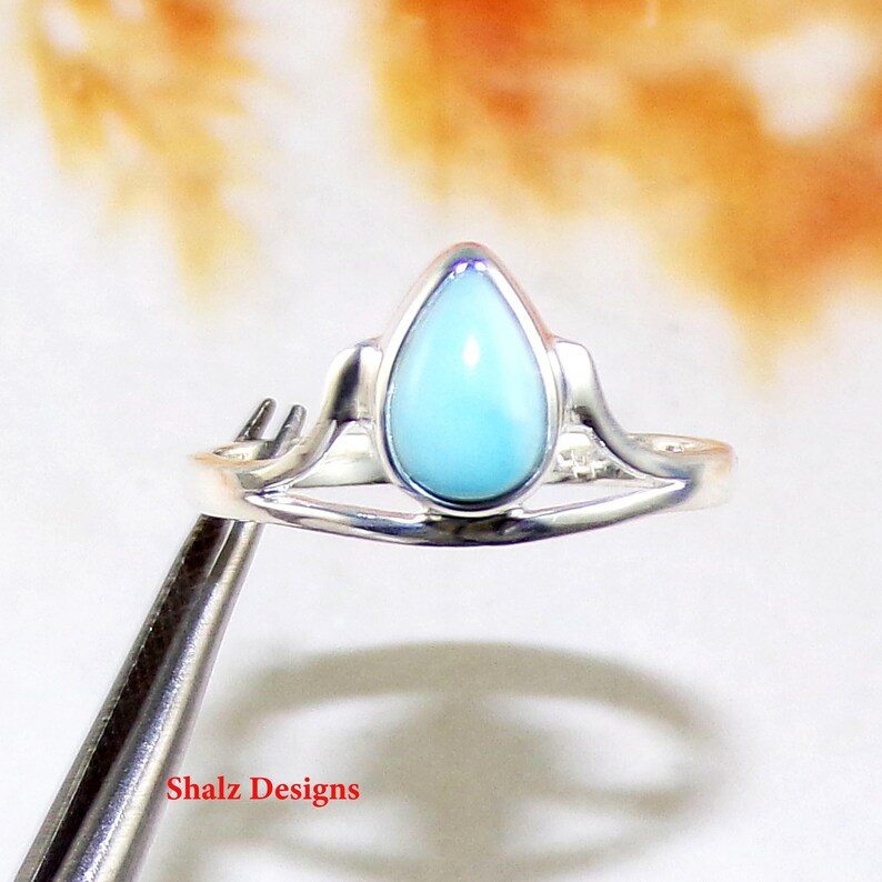 May include: A silver ring featuring a teardrop-shaped blue gemstone. The ring has a delicate, curved design.