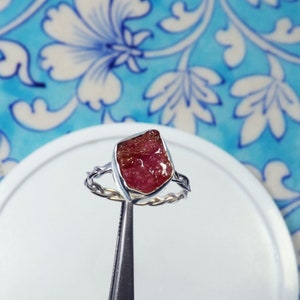May include: A silver ring with a pink and clear raw gemstone set in the centre. The ring has a twisted band.