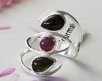 May include: Silver ring featuring three gemstones: a black, a pink, and a green tourmaline. The ring has a curved, open band design.