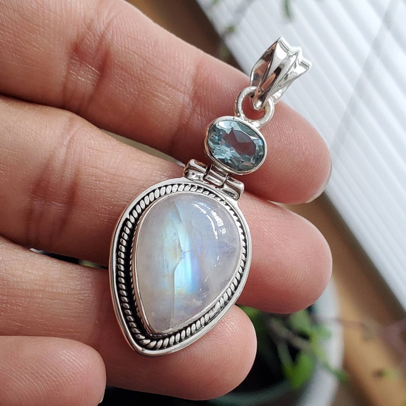 May include: A silver pendant with a teardrop-shaped moonstone and a smaller oval-shaped blue topaz gemstone.