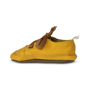 May include: A pair of yellow canvas baby shoes with brown laces. The shoes have a brown rubber sole.