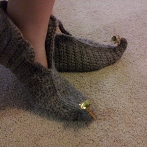 May include: A pair of grey crocheted slippers with bells attached to the toes.